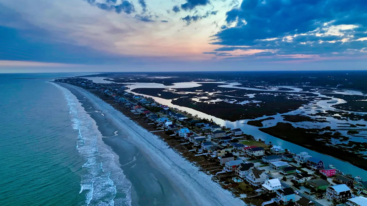 Aerial at dusk of beach houses along the dune line with tidal marsh creeks behind