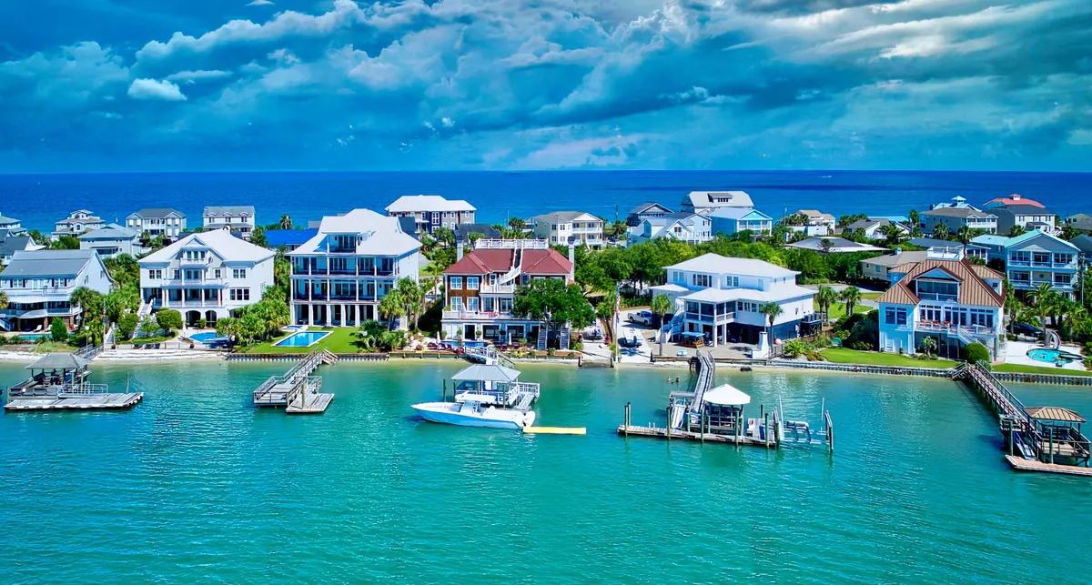 Aerial of waterfront houses with private docks on a turquoise channel, ocean behind